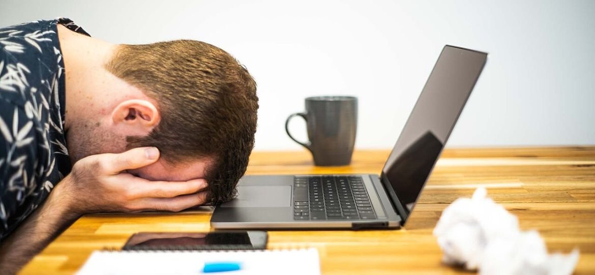 Persona con la testa appoggiata sulla scrivania davanti al laptop, immagine simbolica del burnout lavorativo