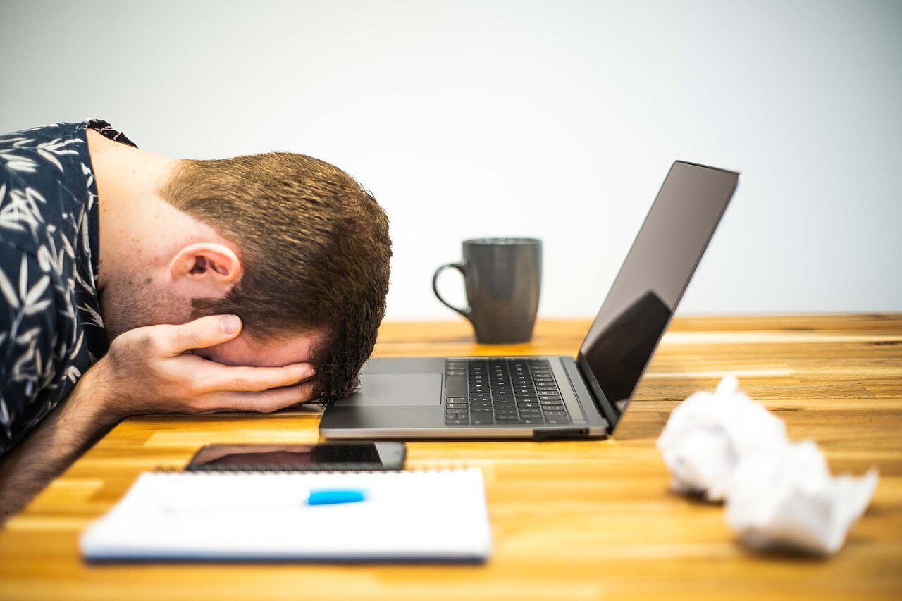 Persona con la testa appoggiata sulla scrivania davanti al laptop, immagine simbolica del burnout lavorativo